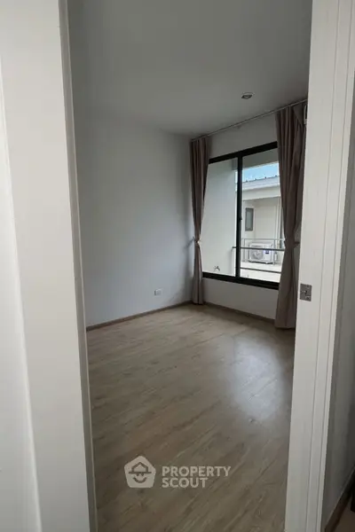 Spacious empty room with wooden flooring and large window, perfect for customization.