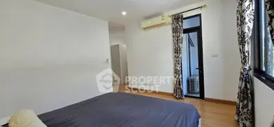 Spacious bedroom with wooden flooring and large window for natural light.