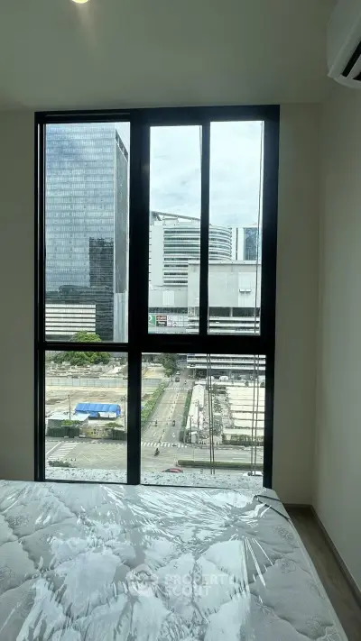 Modern bedroom with large window offering stunning city view in high-rise apartment.