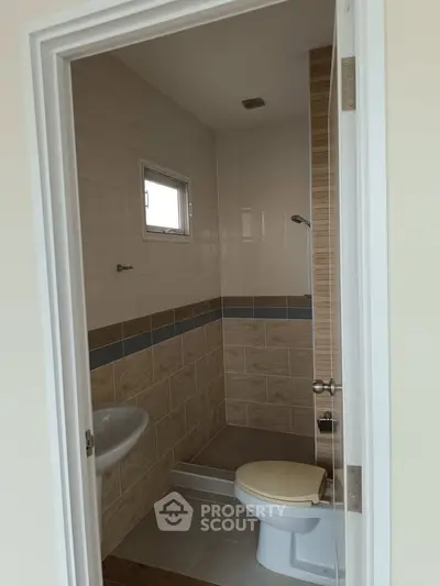 Compact bathroom with tiled walls and small window, featuring a toilet and sink.