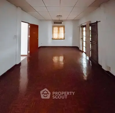 Spacious empty living room with wooden flooring and natural light.