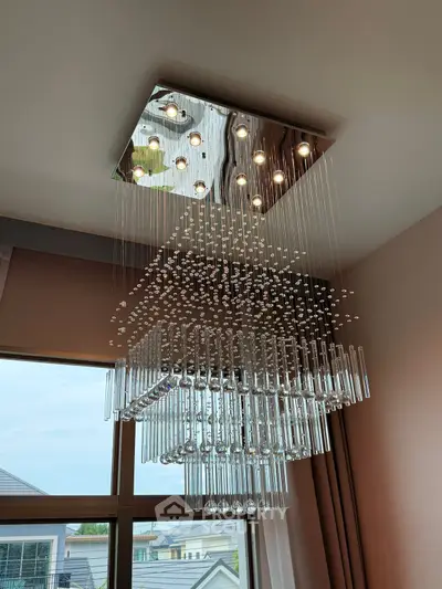 Luxurious modern chandelier in elegant living room with large windows and stylish curtains.
