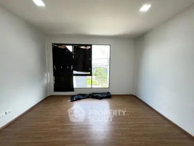 Spacious empty room with wooden flooring and large window.