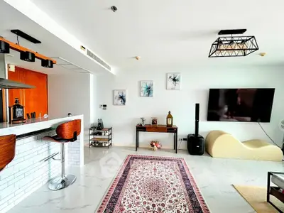 Modern living room with stylish decor, open kitchen layout, and large flat-screen TV.