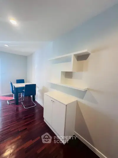 Modern dining area with sleek white shelves and stylish blue chairs on polished wooden floor.
