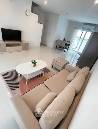 Modern living room with beige sofa, flat-screen TV, and stylish decor in a bright, open space.