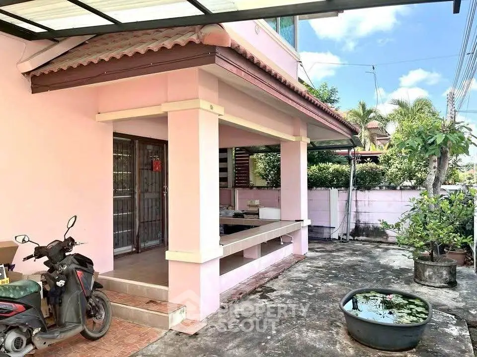 Charming pink house exterior with covered porch and lush garden view.