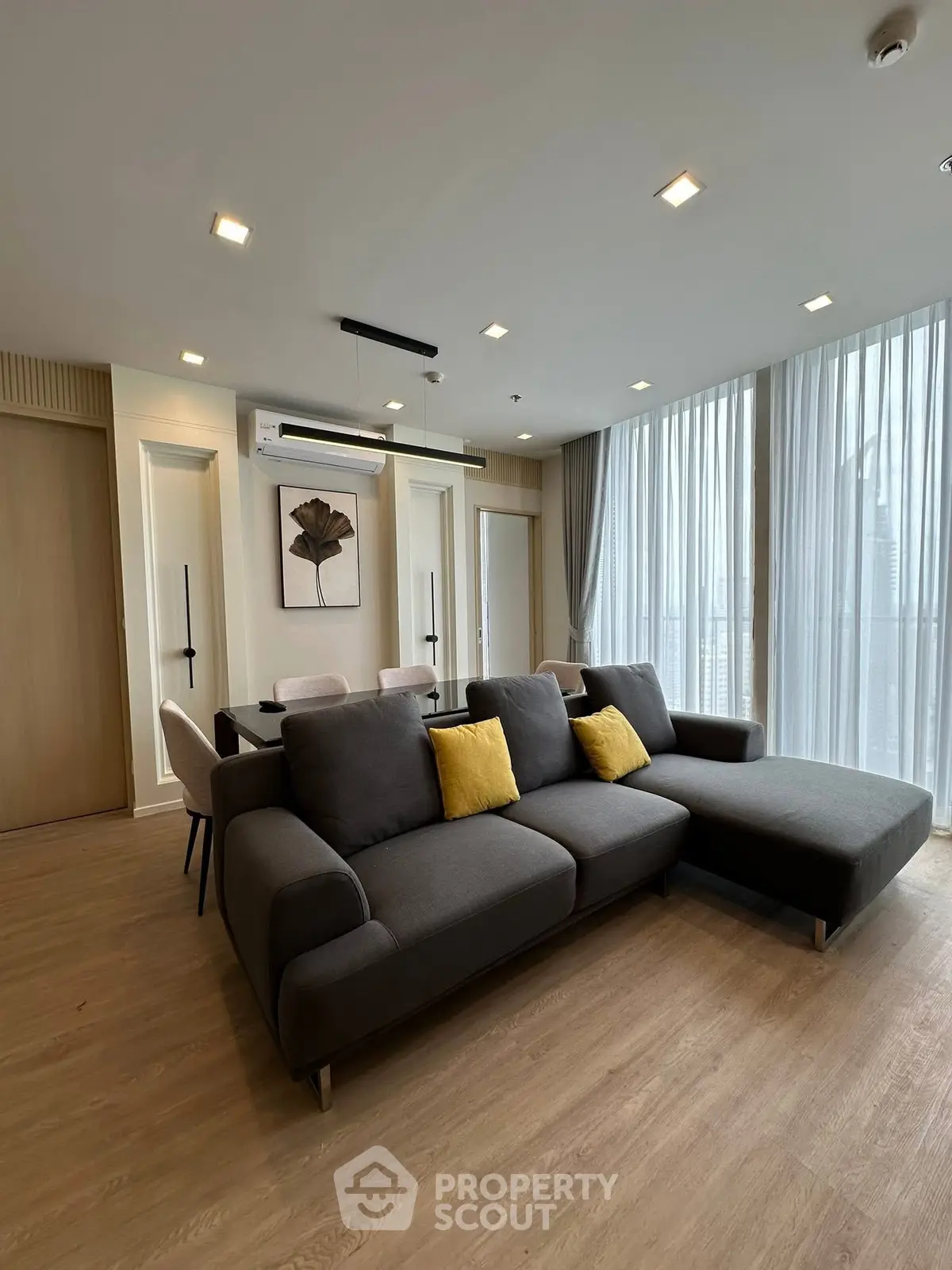 Spacious modern living room with large sofa and dining area, featuring floor-to-ceiling windows.