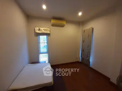 Minimalist bedroom with wooden flooring and air conditioning unit.