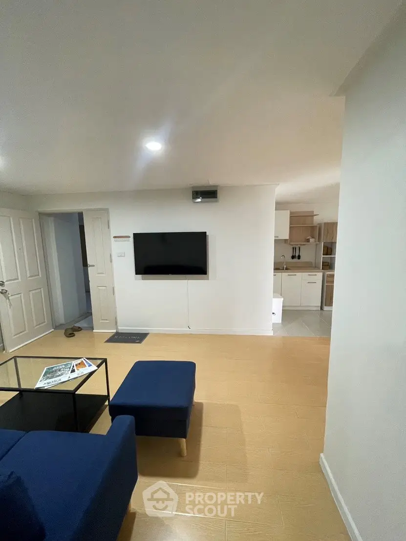 Modern living room with sleek TV setup and cozy seating area, leading to a stylish kitchen.