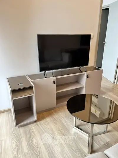 Modern living room with sleek TV stand and glass coffee table on wooden flooring.