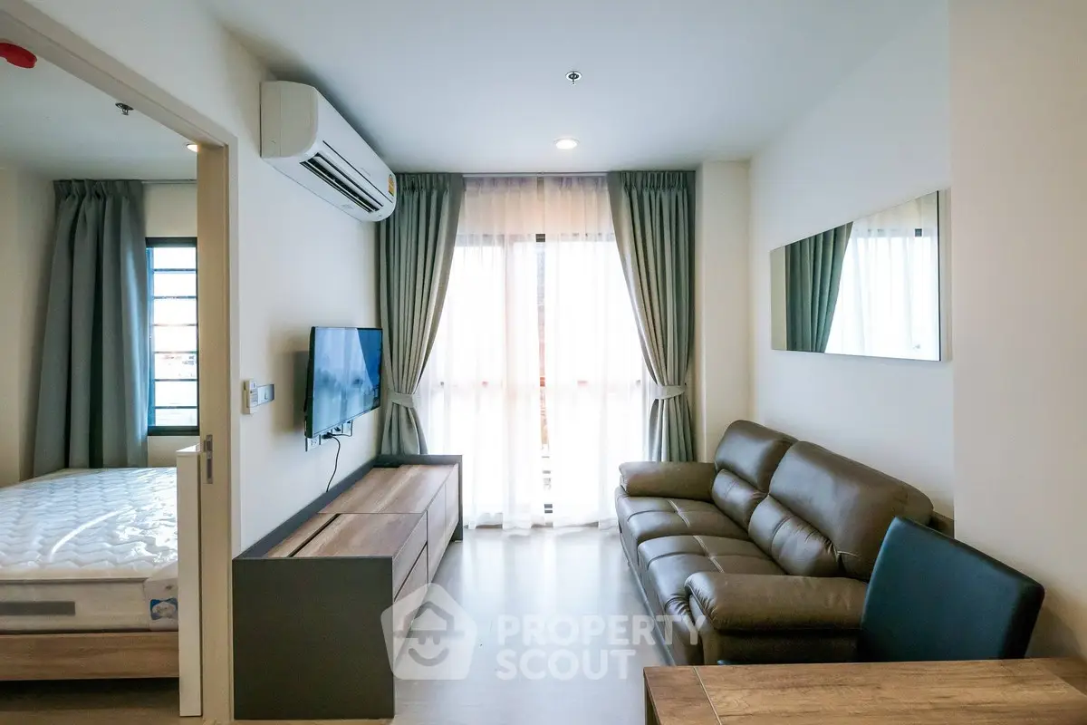 Modern living room with leather sofa, wall-mounted TV, and natural light from large window.