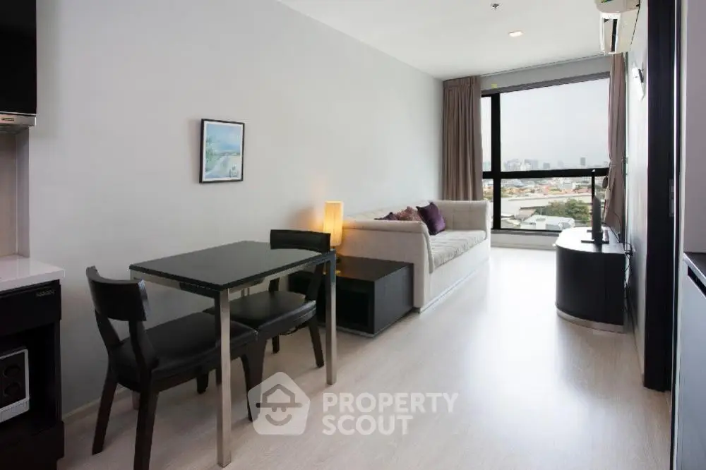 Modern living room with sleek furniture and large window offering city views.