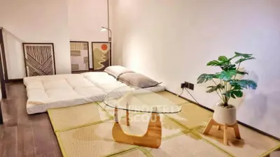 Stylish minimalist living room with futon, modern art, and glass coffee table on tatami mat.
