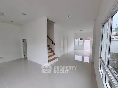Spacious modern living room with large windows and sleek staircase in a bright, open layout.