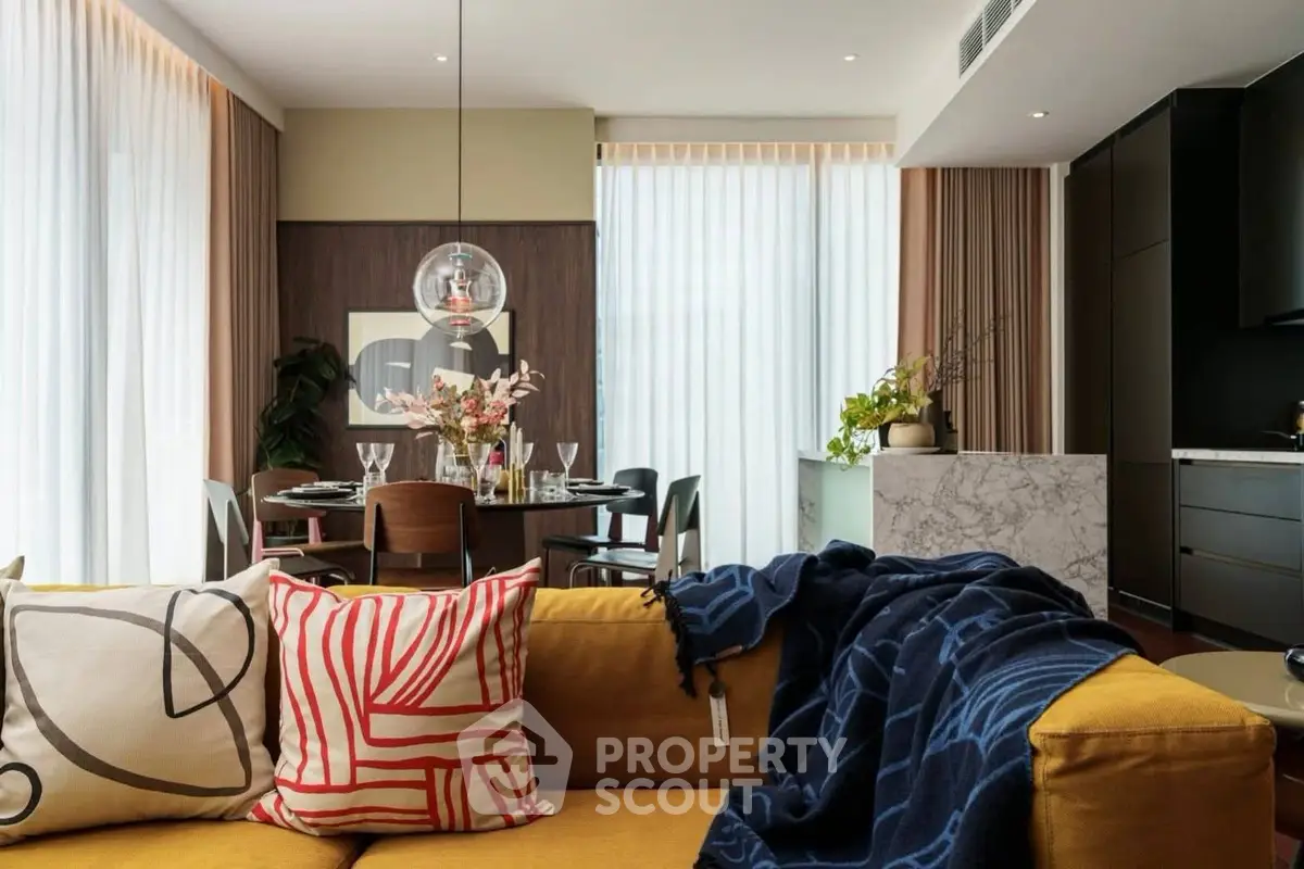 Modern living room with stylish decor and open kitchen layout, featuring a cozy yellow sofa and elegant dining area.