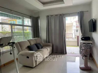 Modern living room with large windows, cozy sofa, and treadmill, opening to a patio with garden view.