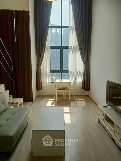 Spacious living room with high ceilings and large windows offering natural light and city views.