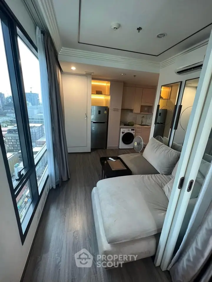 Modern living room with city view, featuring cozy sofa and compact kitchen area.