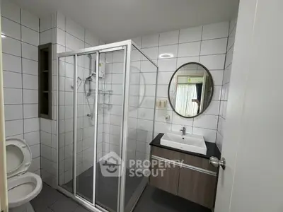 Modern bathroom with glass shower and sleek vanity in contemporary apartment.