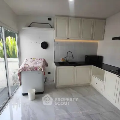 Modern kitchen with sleek cabinets and natural light, featuring a compact washing machine and elegant marble flooring.