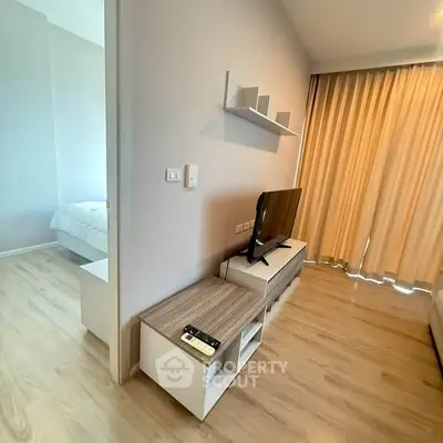Modern living room with TV and wooden flooring, adjacent to a cozy bedroom.
