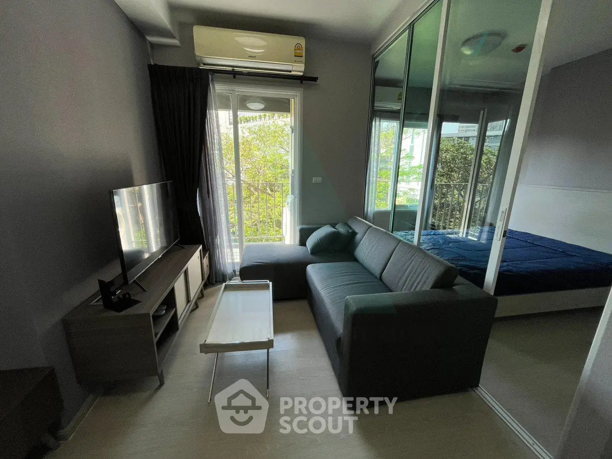Modern living room with sleek furniture and natural light, adjacent to a cozy bedroom with glass partition.