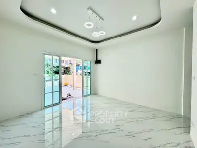 Spacious modern living room with marble flooring and stylish ceiling lights, opening to a bright outdoor area.