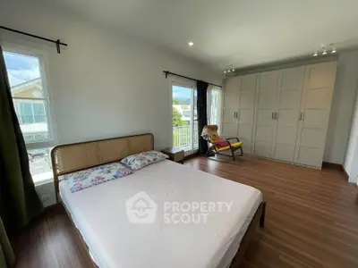Spacious bedroom with large windows and modern wardrobe, featuring a cozy chair and wooden flooring.