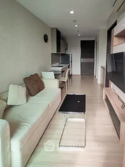 Modern living room with cozy sofa, sleek TV unit, and compact kitchen in open layout apartment.