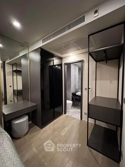 Modern bedroom with sleek black wardrobe and ensuite bathroom, featuring elegant wood flooring and stylish decor.