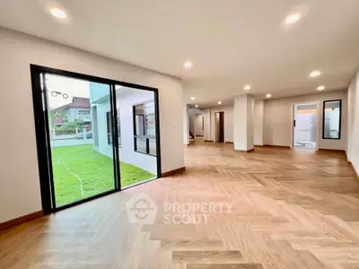Spacious modern living room with wooden flooring and large windows overlooking a lush garden.