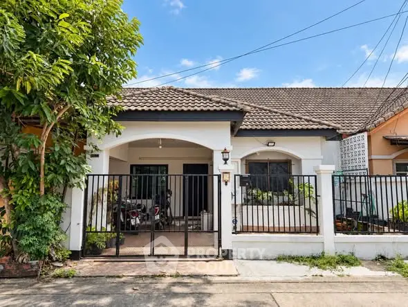 Charming single-story house with gated entrance and lush greenery, perfect for cozy living.