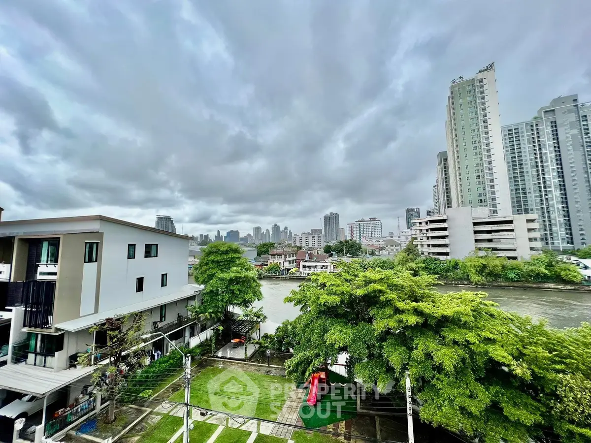 Stunning cityscape view from a high-rise apartment overlooking lush greenery and river.