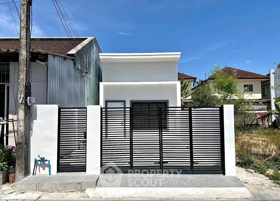 Modern minimalist house exterior with sleek black fence and white facade under clear blue sky.