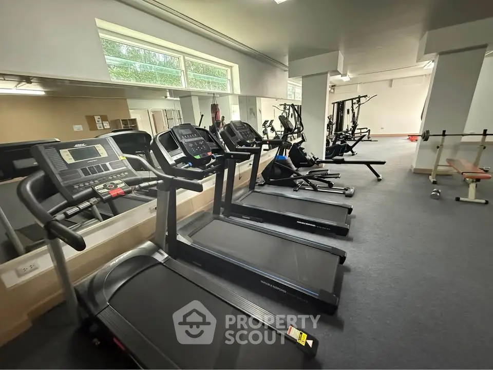 Spacious gym with modern fitness equipment and large mirrors in a residential building.