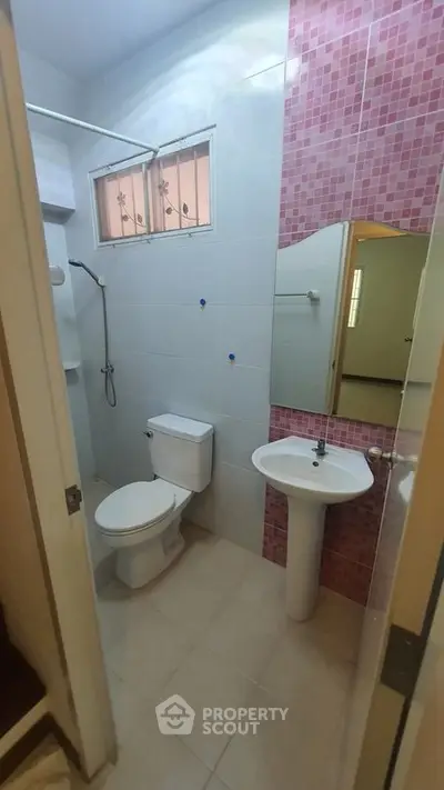 Modern bathroom with pink mosaic tiles and white fixtures in a cozy apartment.