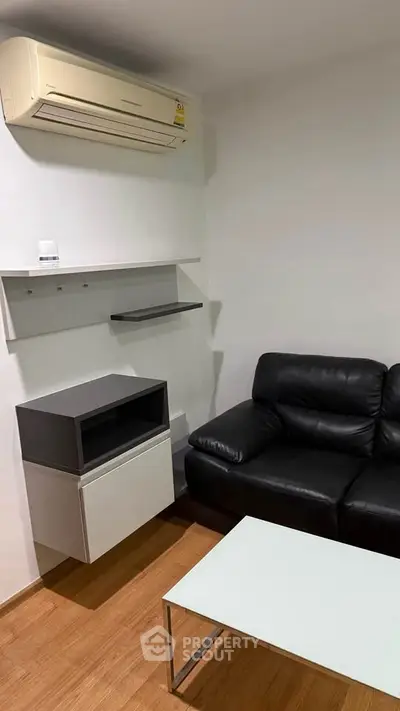 Modern living room with black leather sofa and wall-mounted air conditioner
