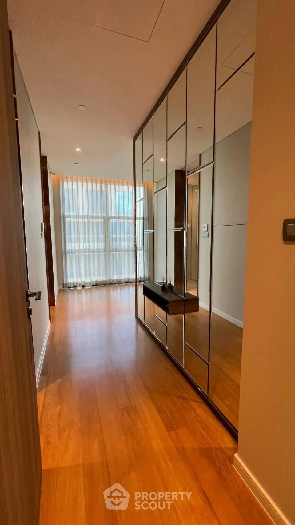 Spacious hallway with elegant wooden flooring and mirrored wall panels in modern apartment.