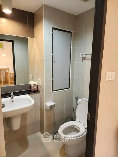 Modern bathroom with sleek fixtures and neutral tiles, featuring a wall-mounted sink and toilet.