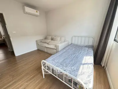 Bright bedroom with wooden flooring, cozy sofa, and air conditioning unit.