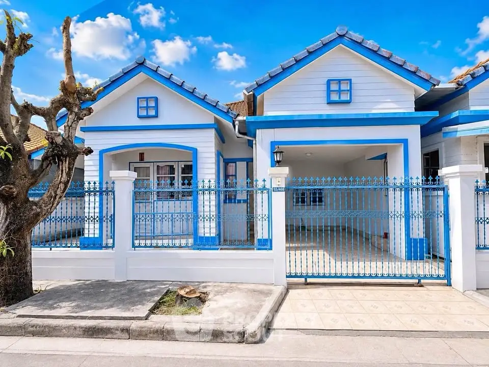 Charming blue and white house with gated entrance and tiled driveway under a clear blue sky.