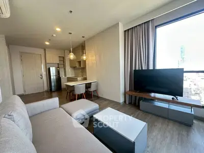 Modern living room with open kitchen and city view, featuring sleek furniture and large window.