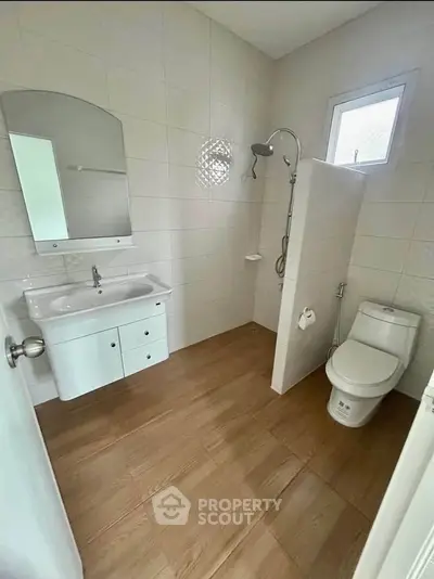 Modern bathroom with sleek fixtures and wooden flooring, featuring a shower and vanity unit.