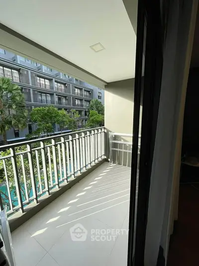 Spacious balcony with modern railing overlooking lush greenery and contemporary building.