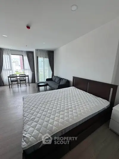 Spacious modern bedroom with large windows and city view, featuring a cozy seating area and dining space.