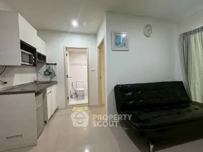 Modern studio apartment with sleek kitchen and cozy living area, featuring a stylish black sofa and wall clock.