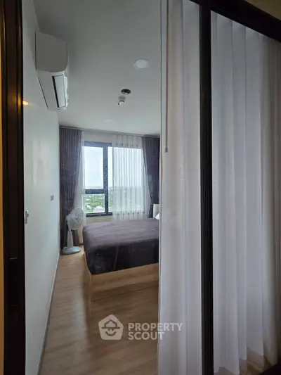 Modern bedroom with large window offering stunning city view, featuring sleek wooden flooring and elegant curtains.