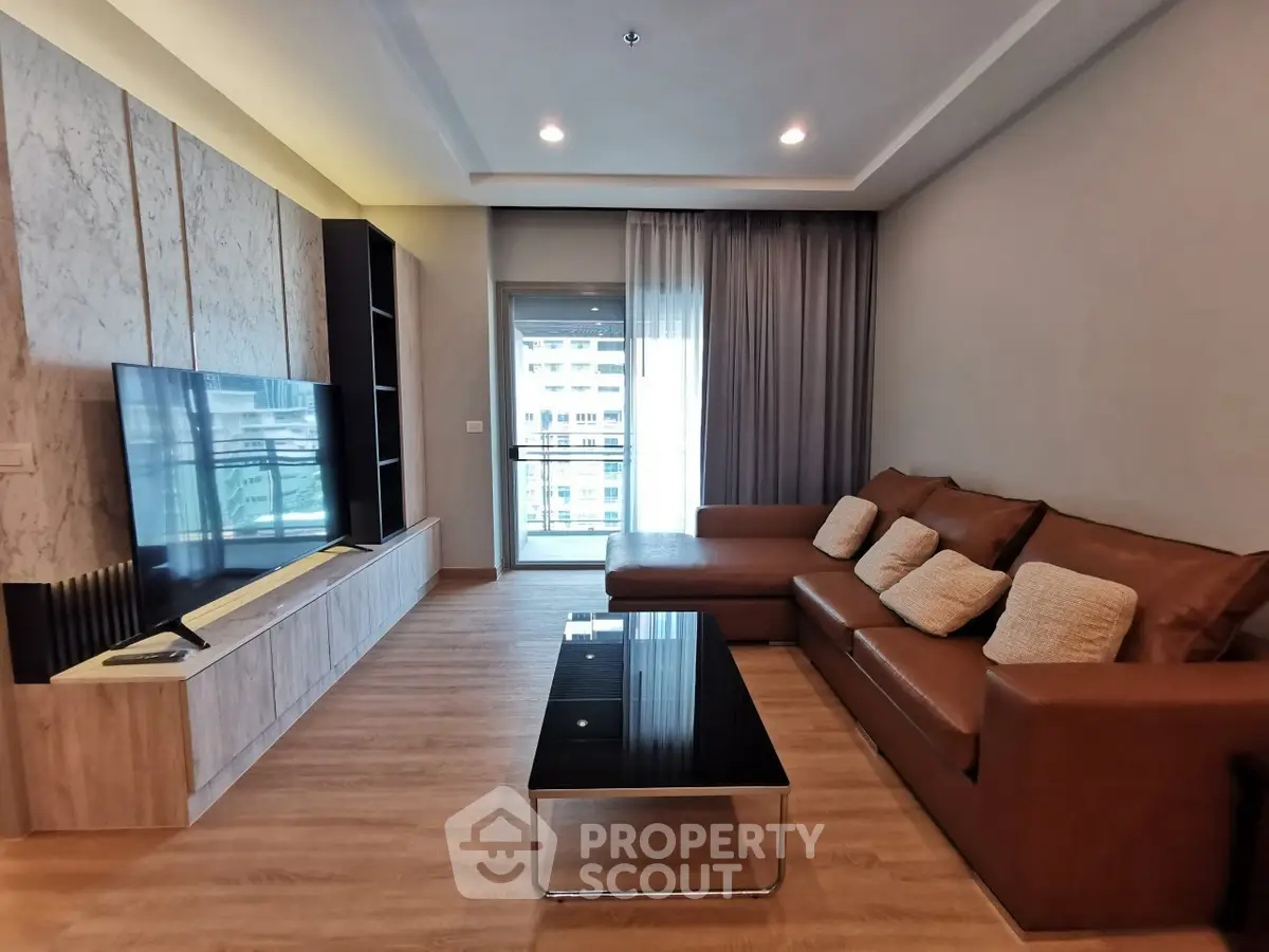 Spacious modern living room with leather sofa and large TV, featuring a balcony view.