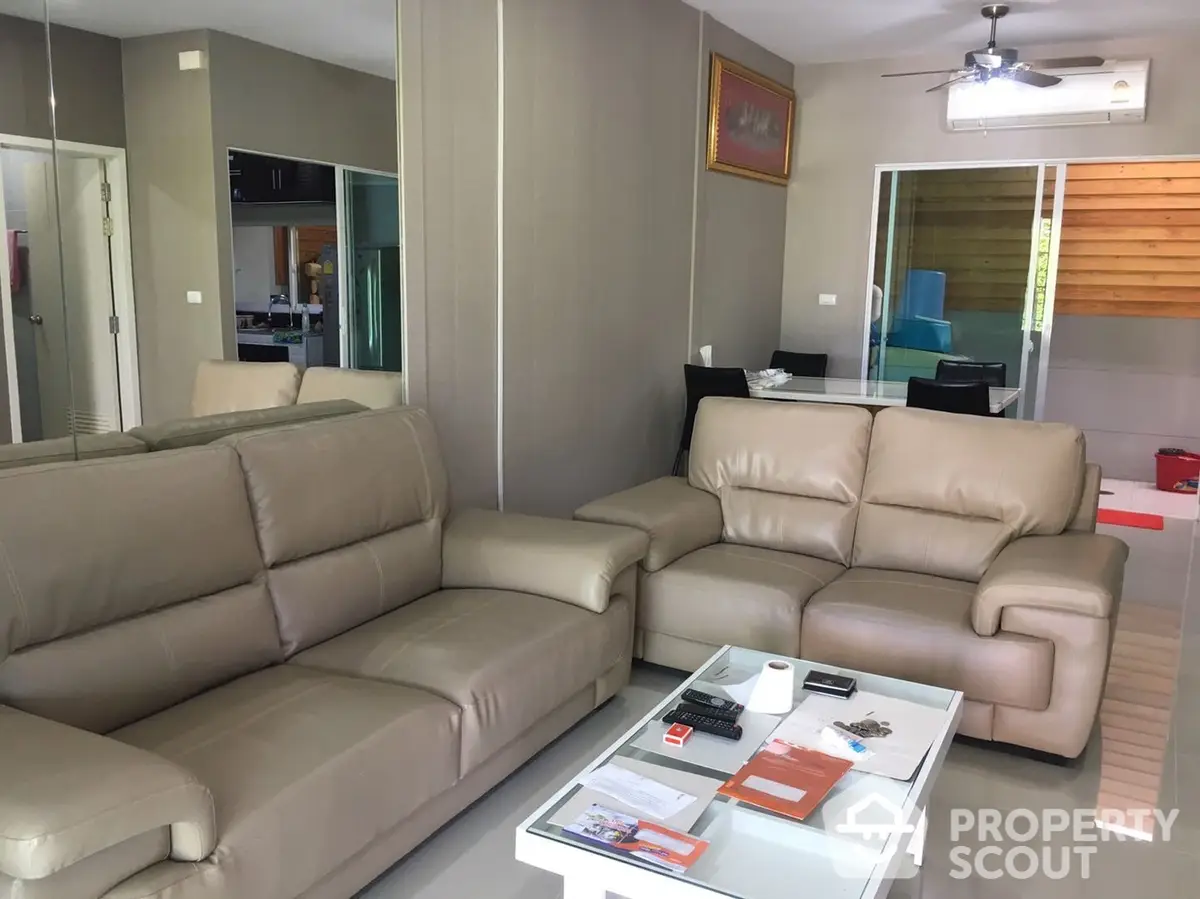 Spacious living room with modern leather sofas, tiled flooring, and an open layout leading to a well-equipped kitchen.